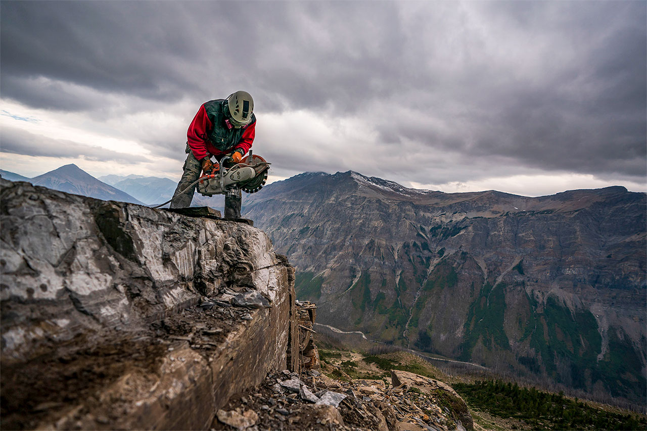 a man standing on a cliff ledge using a rock saw